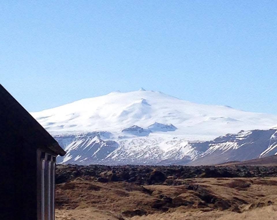 A dark timber building and lava fields beneath a snow-covered mountain in Iceland